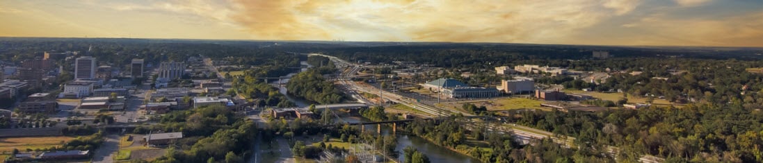 an aerial shot of a gorgeous autumn landscape at Carolyn Crayton Park at sunset with a river, lush green trees and buildings with powerful clouds at sunset in Macon Georgia